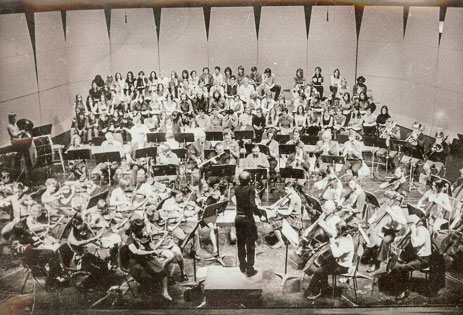An orchestra and choir with a conductor in the centre.